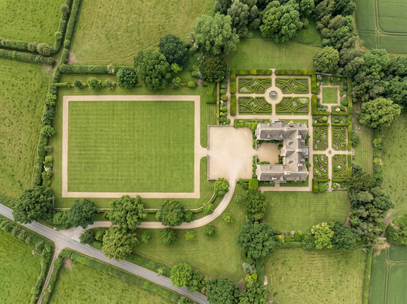 Top-down aerial of a countryside wedding venue with a large open lawn, manor house and formal gardens
